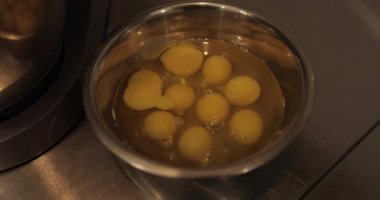 Çiğ tavuk yumurtaları, profesyonel bir pasta mutfağının masasında metal bir kaseye kırılır..