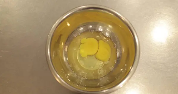Çiğ tavuk yumurtaları, profesyonel bir pasta mutfağının masasında metal bir kaseye kırılır..