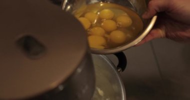 Çiğ tavuk yumurtaları, profesyonel bir pasta mutfağının masasında metal bir kaseye kırılır..