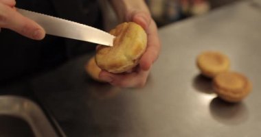 Şekerlemecinin muhallebi ile doldurmak için hazırladığı profiteroller bir tabağa konur. Bir şekerlemecinin kadın elleri eklerlerle başlar..