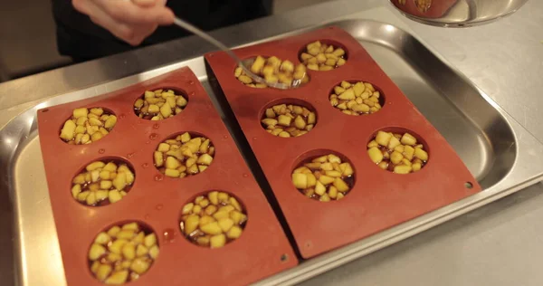 Preparation of apple desserts in a silicone baking tray. Filling a silicone tray with diced apples during the work of a professional confectioner.