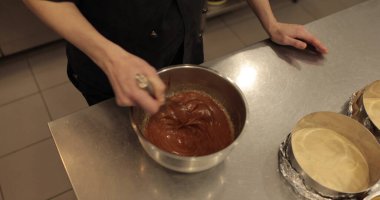 Çikolata jölesini yuvarlak metal bir kâseyle çırpıcıyla karıştırmak. Çikolatalı kremayı çırpıcıyla karıştıran ellerin yakın çekimi. Profesyonel şekerleme..