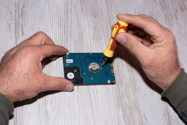 Elleri mavi eldivenli, ahşap bir masada tornavida olan bir adam.