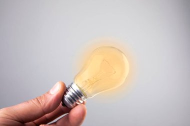 Beyaz arka planda ampullü bir ampulü tutan el..