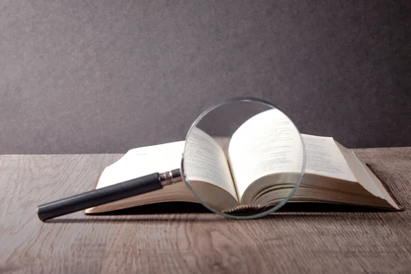 Açık bir kitabın üzerindeki büyüteç.