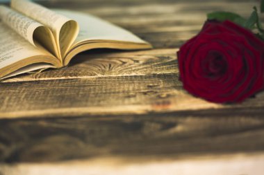 kitap ve kırmızı gül ahşap arka planda