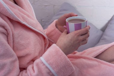 Bornozlu bir kadının ellerinde bir fincan kahve