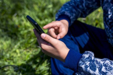 Yakışıklı bir çocuk çimenlerde oturur ve telefona bakar.