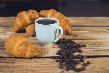 Bir fincan kahve, kruvasan ve ahşap duvar.