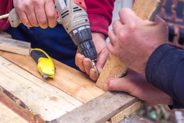 Kablosuz matkapla tahta plakayı vidalayan bir adam.
