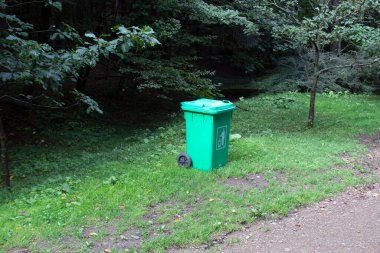 Ormanda yeşil çimlerin üzerindeki çöp tenekesi.