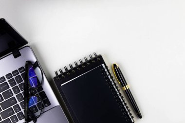 Bilgisayarlı, defterli, gözlüklü ve kalemli modern çalışma alanının beyaz arkaplanlı üst görünümü.