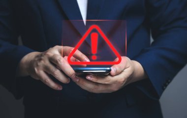İşadamı elinde uyarı işareti olan akıllı telefon kullanıyor. İş ve tehlike kavramı..