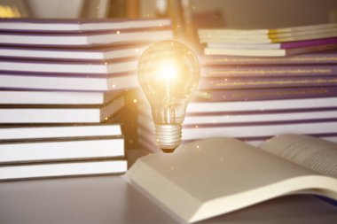 Ampul açık bir kitapta, kitap yığını ve ahşap masanın üzerinde. bilgi, eğitim veya öğrenme kavramı.