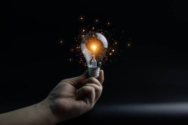 Karanlık arka planda parlayan ampullü el, yakın plan.