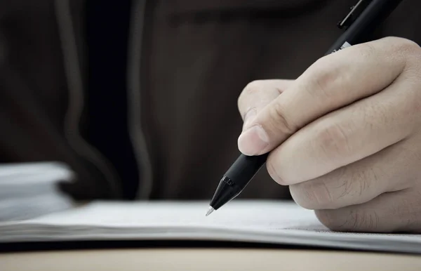 man in a black jacket writes a letter in notebook