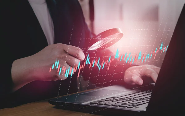 Monitoring and analysis of stock charts in the digital market. Businessmen use a magnifying glass to analyze sales data and economic growth along with foreign exchange trading.