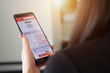 Otel hizmetlerinden müşteri memnuniyetini değerlendirmek. Akıllı telefon kullanan kadın müşteri çok iyi bir tatmin notu verdi ve otelin internet uygulaması tarafından sağlanan hizmetler hakkında tavsiye verdi