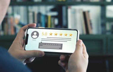 Müşteri memnuniyeti anketi. Smartphone kullanan bir adam yorum yaparak 5 yıldız veriyor. Müşteri hizmetleri ürünlerinin kalitesini değerlendirme kavramı. Memnuniyet Değerlendirmesi En iyi kalite