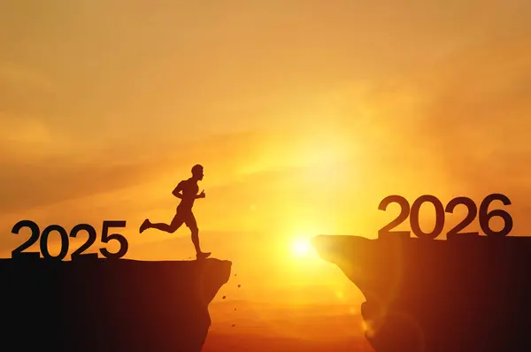 Yeni Yıl 2026, ilham ve yeni başarı yolunda ilerleme. İnsan siluetleri uçurumdan bitiş çizgisine doğru atlıyor. Yeni yıl 2026 günbatımında güzel bir yazı.