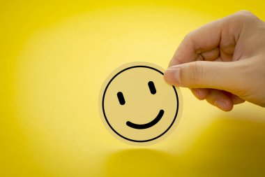 Sarı arka planda gülen surat ifadesi olan bir daire kağıdı tutuyorum. Müşteri geribildirim değerlendirmesi kavramı, en yüksek tatmin oranını verir.