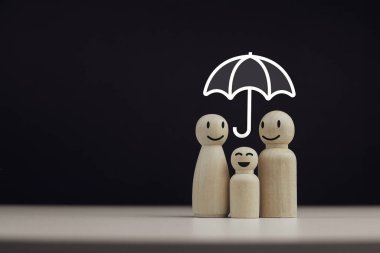 Aileyi maddi ve manevi açıdan korumak ve korumak için sigorta koruması kavramı. Kopya alanı olan ahşap bebekler ailesinin şemsiye simgesi.