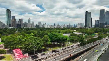 Time-lapse of traffic on a city street and green spaces of a park with the many skyscrapers in the background of the central business district of Thailand. horizontal footage