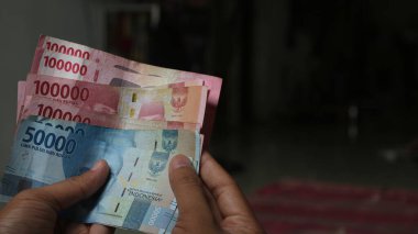 Surabaya, Endonezya. 01-15-2025: İşlemler, taksitler halinde ödemeler - sigorta, krediler ve satın almalar için elde tutulan birkaç rupiah banknotu. - Evet. Ramazan Bayramı.
