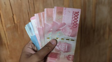 Surabaya, Endonezya. 01-15-2025: İşlemler, taksitler halinde ödemeler - sigorta, krediler ve satın almalar için elde tutulan birkaç rupiah banknotu. - Evet. Ramazan Bayramı.
