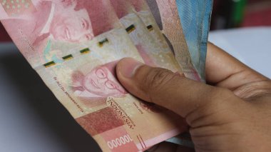 Surabaya, Endonezya. 01-15-2025: İşlemler, taksitler halinde ödemeler - sigorta, krediler ve satın almalar için elde tutulan birkaç rupiah banknotu. - Evet. Ramazan Bayramı.