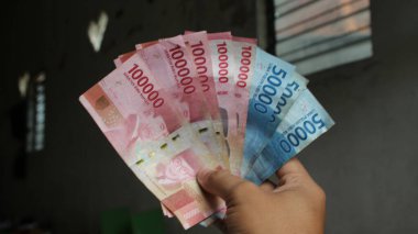 Surabaya, Endonezya. 01-15-2025: İşlemler, taksitler halinde ödemeler - sigorta, krediler ve satın almalar için elde tutulan birkaç rupiah banknotu. - Evet. Ramazan Bayramı.