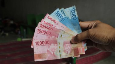 Surabaya, Endonezya. 01-15-2025: İşlemler, taksitler halinde ödemeler - sigorta, krediler ve satın almalar için elde tutulan birkaç rupiah banknotu. - Evet. Ramazan Bayramı.