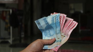 Surabaya, Endonezya. 01-15-2025: İşlemler, taksitler halinde ödemeler - sigorta, krediler ve satın almalar için elde tutulan birkaç rupiah banknotu. - Evet. Ramazan Bayramı.