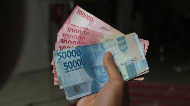 Surabaya, Endonezya. 01-15-2025: İşlemler, taksitler halinde ödemeler - sigorta, krediler ve satın almalar için elde tutulan birkaç rupiah banknotu. - Evet. Ramazan Bayramı.