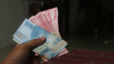 Surabaya, Endonezya. 01-15-2025: İşlemler, taksitler halinde ödemeler - sigorta, krediler ve satın almalar için elde tutulan birkaç rupiah banknotu. - Evet. Ramazan Bayramı.