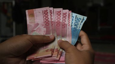 Surabaya, Endonezya. 01-15-2025: İşlemler, taksitler halinde ödemeler - sigorta, krediler ve satın almalar için elde tutulan birkaç rupiah banknotu. - Evet. Ramazan Bayramı.