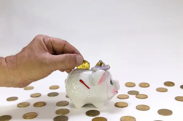 El, etrafına bozuk paralar saçılmış şirin bir domuz kumbarasına bozuk para koyuyor. Finans ve tasarruf kavramı.
