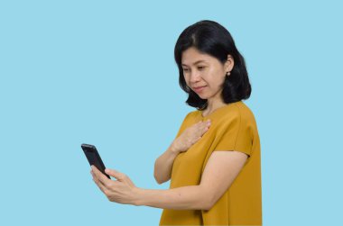 Heyecanlı Asyalı bir kadın elinde bir akıllı telefon tutarken gülümsüyor, mavi bir arka planda soyutlanmış.