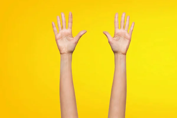 Close-up of right and left hands making a gesture calling for help, isolated on a yellow background.