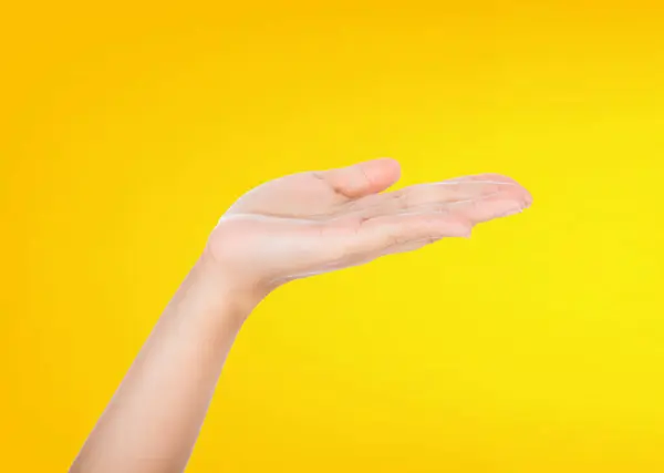 A powerful male hand with an outstretched palm is symbolically presenting an imaginary product in an advertising concept targeted towards women. The scene is isolated on a vibrant yellow background.