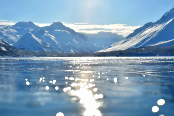 reflection of the sun in the water of a frozen lake with mountains in the background