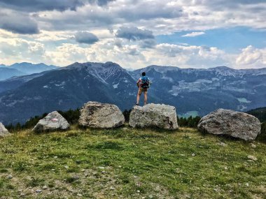 Sırt çantalı bir adam dağın tepesindeki bir kayanın manzarasının tadını çıkarıyor.