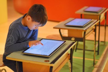 Çocuk kütüphanede tabletle oynuyor.