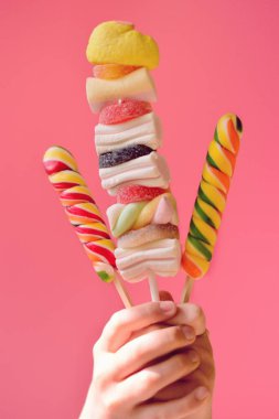 Renkli arka planda farklı renkli lolipopları olan kadın eli 