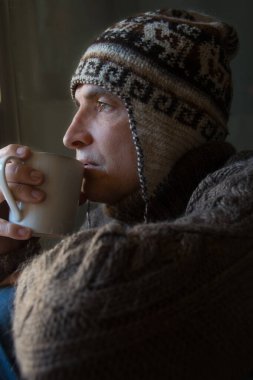 Genç adam pencerede oturuyor ve kahve içiyor, kış zamanı, Noel konsepti.