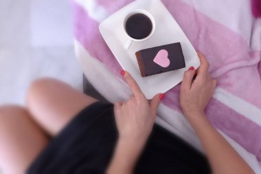 Bir fincan kahve ve üzerine kalp çizilmiş çikolatalı kek olan bir kadın.