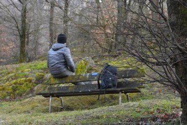 Sırt çantalı genç turist ormandaki ahşap bankta oturuyor.