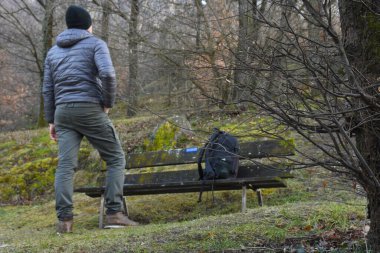 Sırt çantalı genç turist ormandaki ahşap bankta oturuyor.