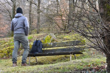 Sırt çantalı genç turist ormandaki ahşap bankta oturuyor.