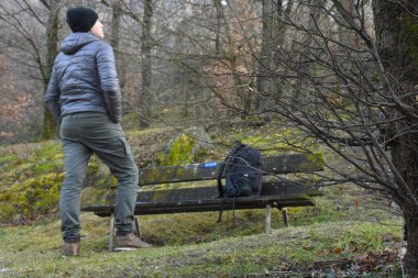 Sırt çantalı genç turist ormandaki ahşap bankta oturuyor.